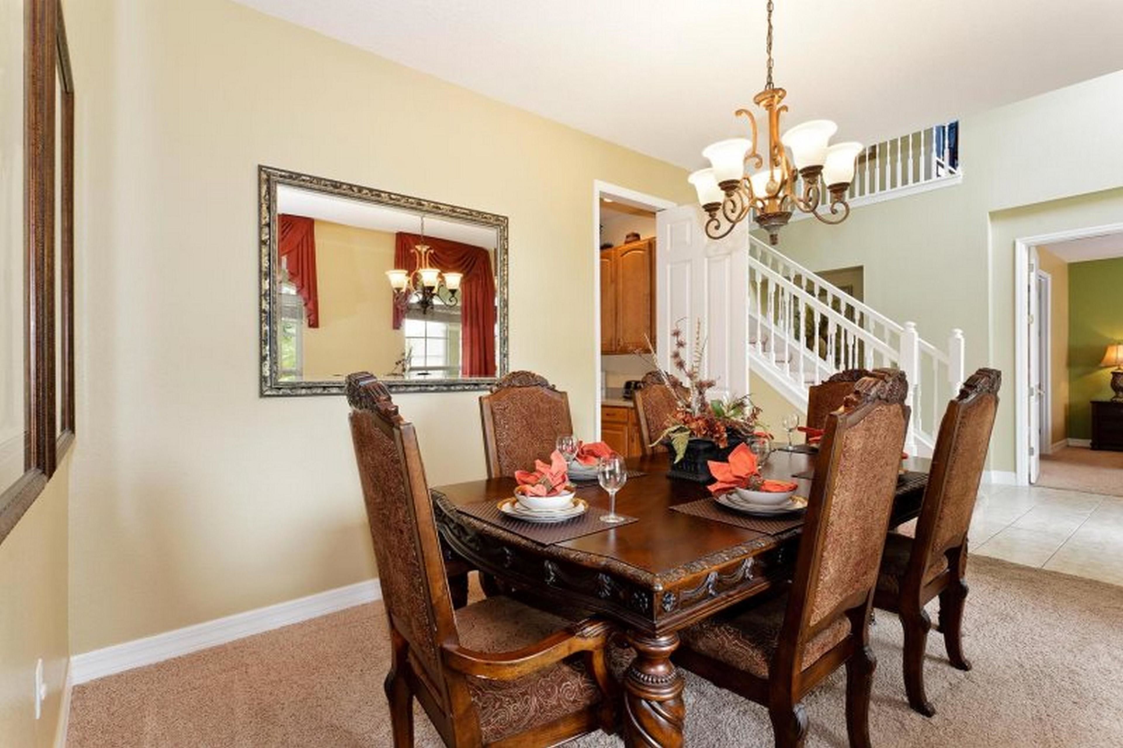A dining room with a large wooden table, four chairs, a chandelier, and a mirror on the wall.
