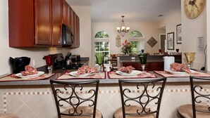 A kitchen with wooden cabinets, a microwave, and a dining area with a bar. - Formosa Gardens Homes by Atlas VH (Kissimmee)