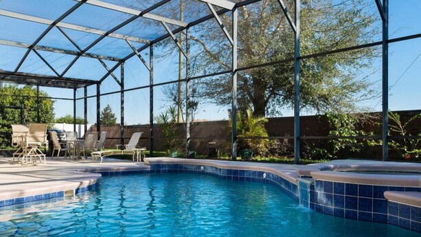 A swimming pool with a glass enclosure, surrounded by lounge chairs and a brick wall. - Formosa Gardens Homes by Atlas VH (Kissimmee)
