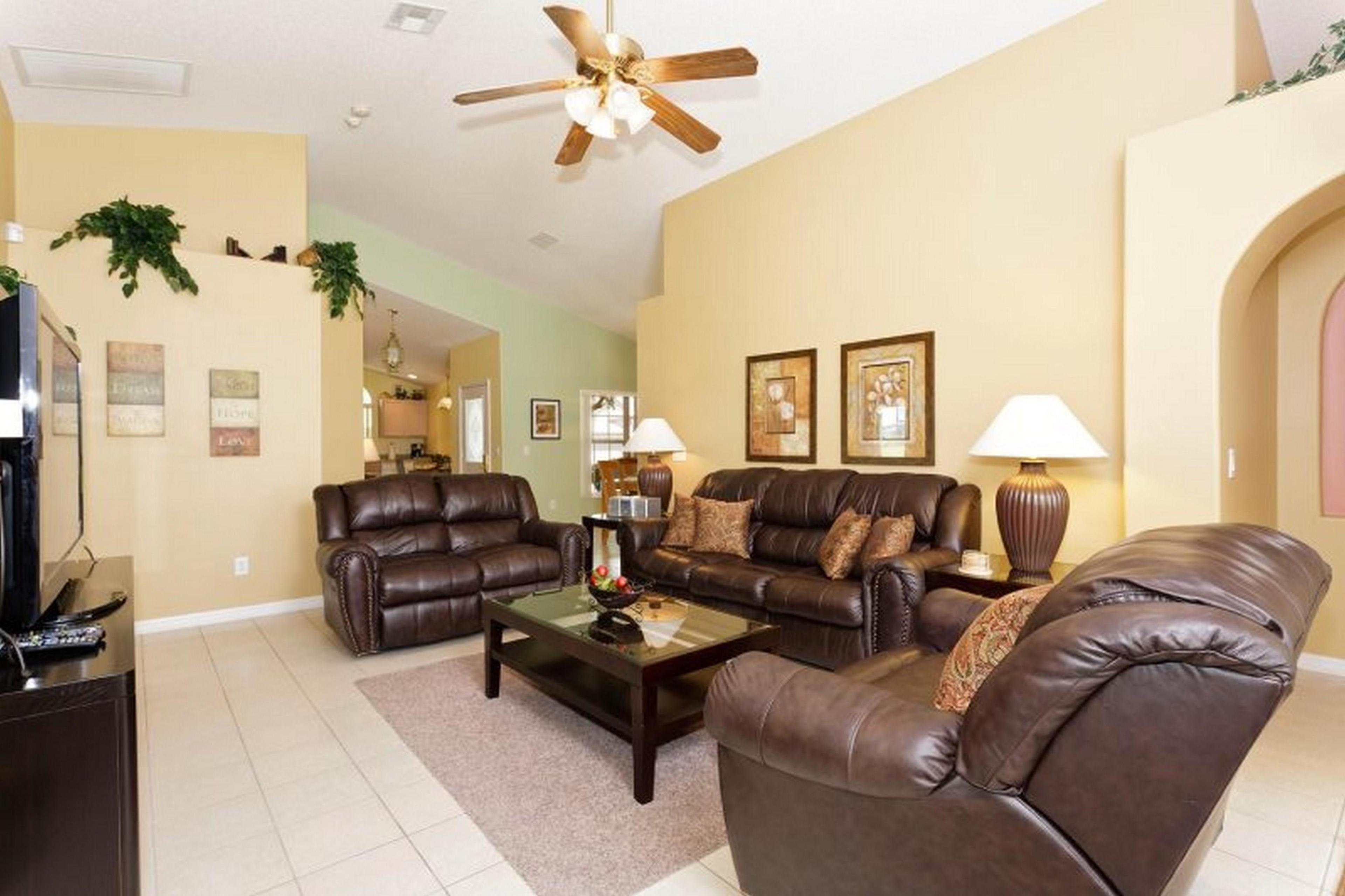 A living room with leather sofas, a coffee table, and a ceiling fan.