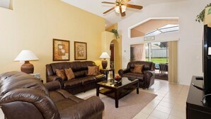 A living room with leather sofas, a coffee table, lamps, and a ceiling fan. - Indian Creek Homes by Atlas VH (Kissimmee)