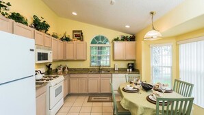 A kitchen with a dining table set for two, a stove, microwave, and cabinets. - Indian Creek Homes by Atlas VH (Kissimmee)