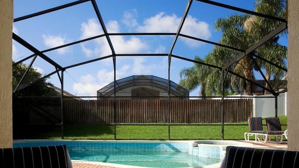 A covered outdoor swimming pool with a view of a house and palm trees in the background. - Indian Creek Homes by Atlas VH (Kissimmee)