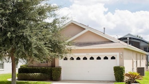 A single-story house with a beige exterior, a white garage door, and a well-maintained lawn. - Indian Creek Homes by Atlas VH (Kissimmee)