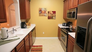 A compact kitchen with wooden cabinets, a stainless steel refrigerator, and a microwave. - Vista Cay Homes by Atlas VH (Orlando)