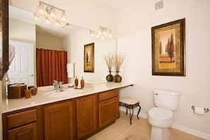 Une salle de bain avec un grand miroir, un lavabo, des toilettes et deux tableaux encadrés accrochés au mur.