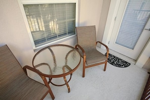 Un petit espace patio avec une table ronde en verre et deux chaises en osier.