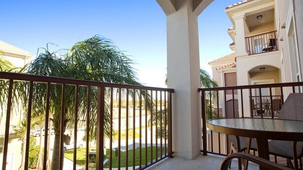 A balcony with a table and chairs, overlooking a well-maintained lawn and palm trees. - Vista Cay Homes by Atlas VH (Orlando)