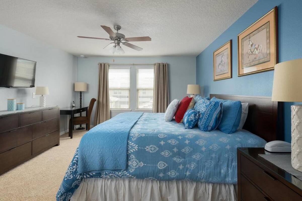 A bedroom with a bed, a desk, a chair, a television, and a ceiling fan.