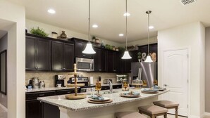 Une cuisine moderne avec des meubles de couleur sombre, un plan de travail en granit, un îlot central doté de tabourets de bar et un éclairage suspendu.