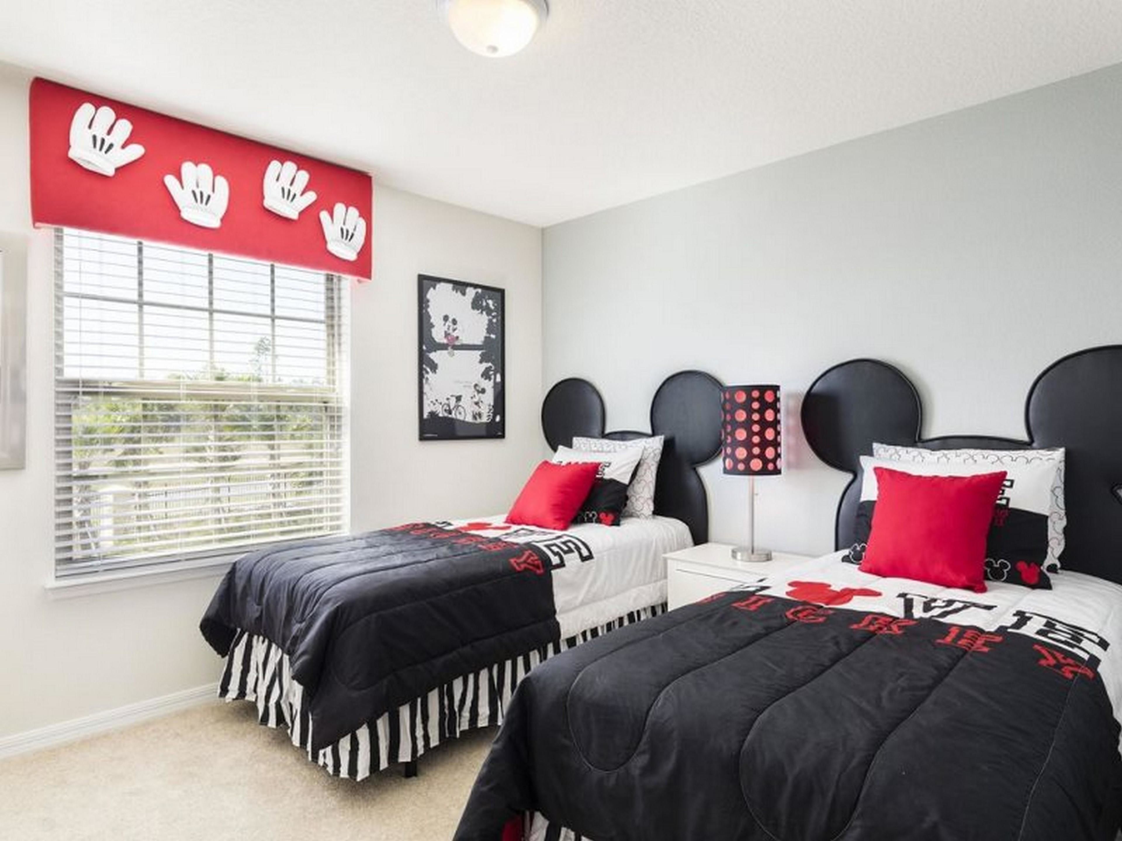 A bedroom with two beds, a window with blinds, a red wall decoration, and a framed picture on the wall.