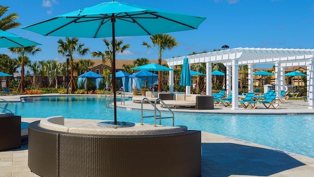Un espace piscine équipé de chaises longues, de parasols et d’un coin salon abrité.