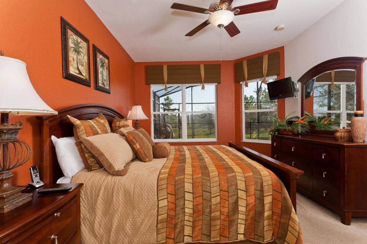 Ein Schlafzimmer mit einem großen Bett, einem Deckenventilator, einem Fernseher und einer Kommode.