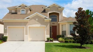 A two-story house with a beige exterior, a red door, and two garage doors. - Windsor Hills Resort Homes by Atlas VH (Kissimmee)