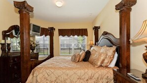 A bedroom with a large bed, a dresser, a mirror, and a window with a view of a fence. - Windsor Hills Resort Homes by Atlas VH (Kissimmee)