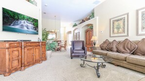 A spacious living room with a large TV, a leather armchair, a glass coffee table, and a sofa with decorative pillows. - Windsor Palms Resort (Kissimmee)