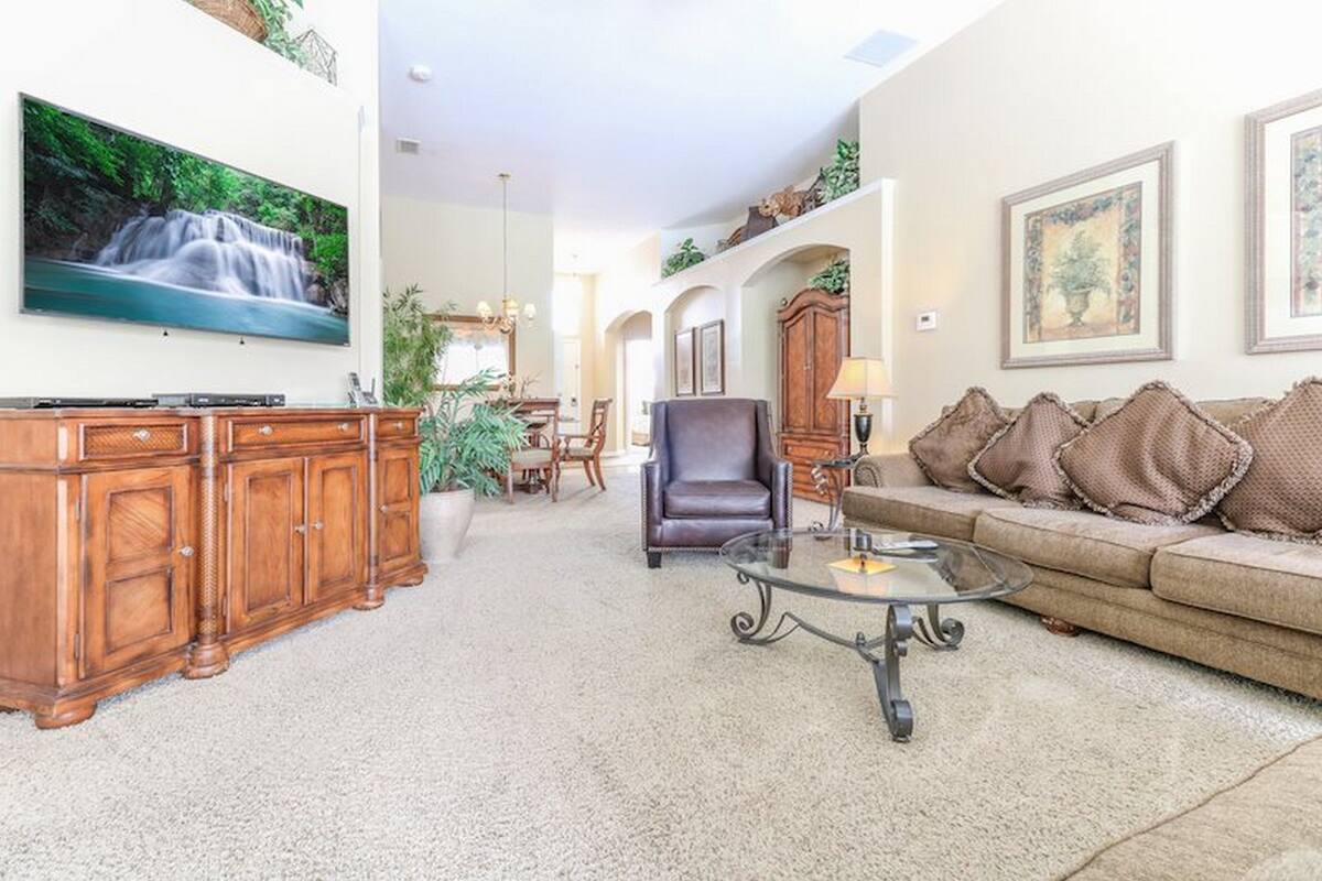 A spacious living room with a large TV, a leather armchair, a glass coffee table, and a sofa with decorative pillows.