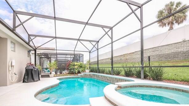 A covered outdoor swimming pool with a glass enclosure, surrounded by a landscaped garden and a stone wall. - Windsor Palms Resort (Kissimmee)