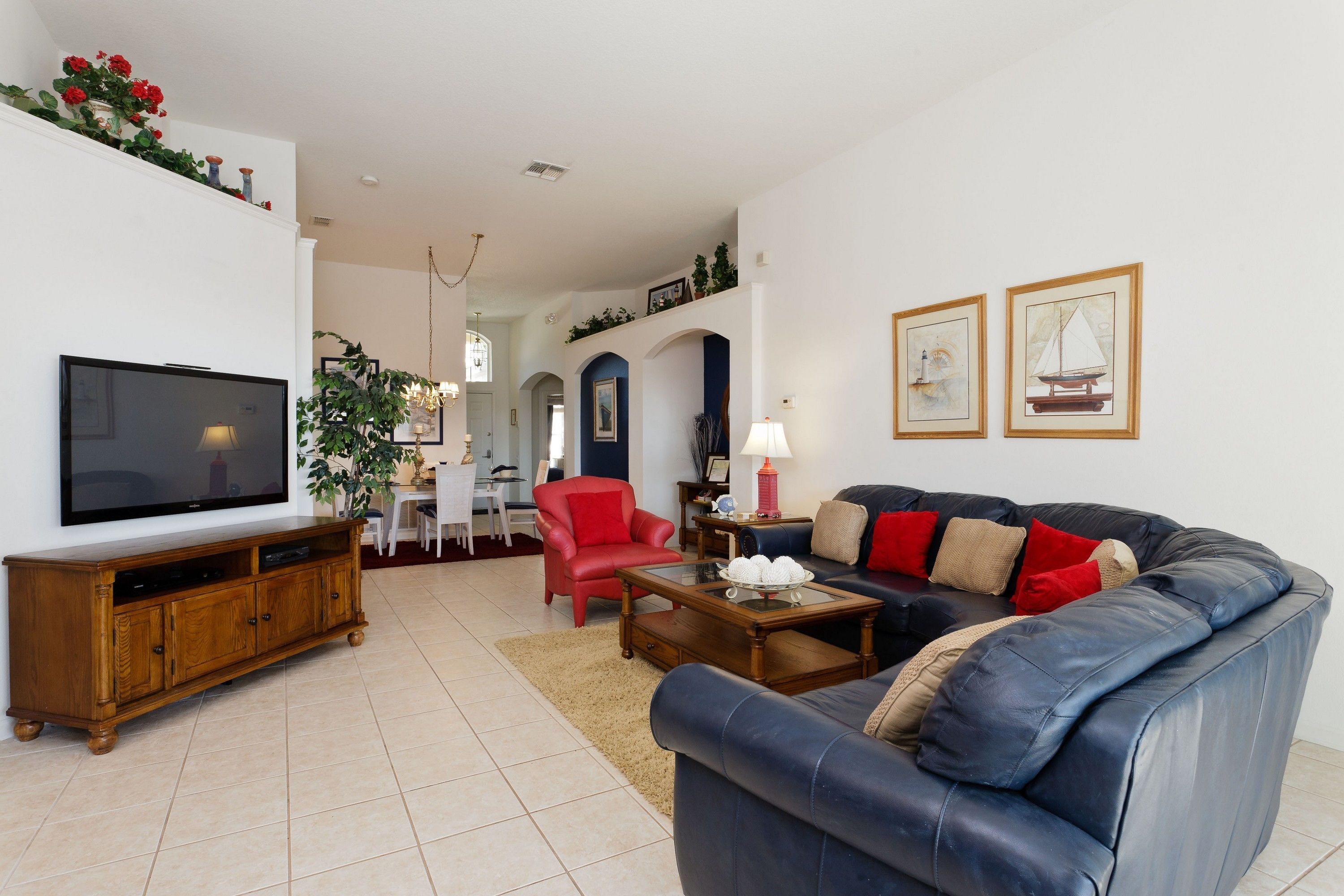 A living room with a television, sofa, red chair, coffee table, and a dining area in the background.