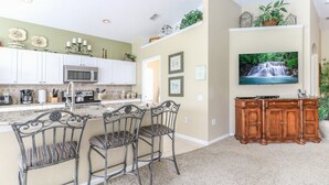 A kitchen with white cabinets, a microwave, and a coffee maker. There is a dining area with metal chairs and a TV on the wall. - Windsor Palms Resort (Kissimmee)