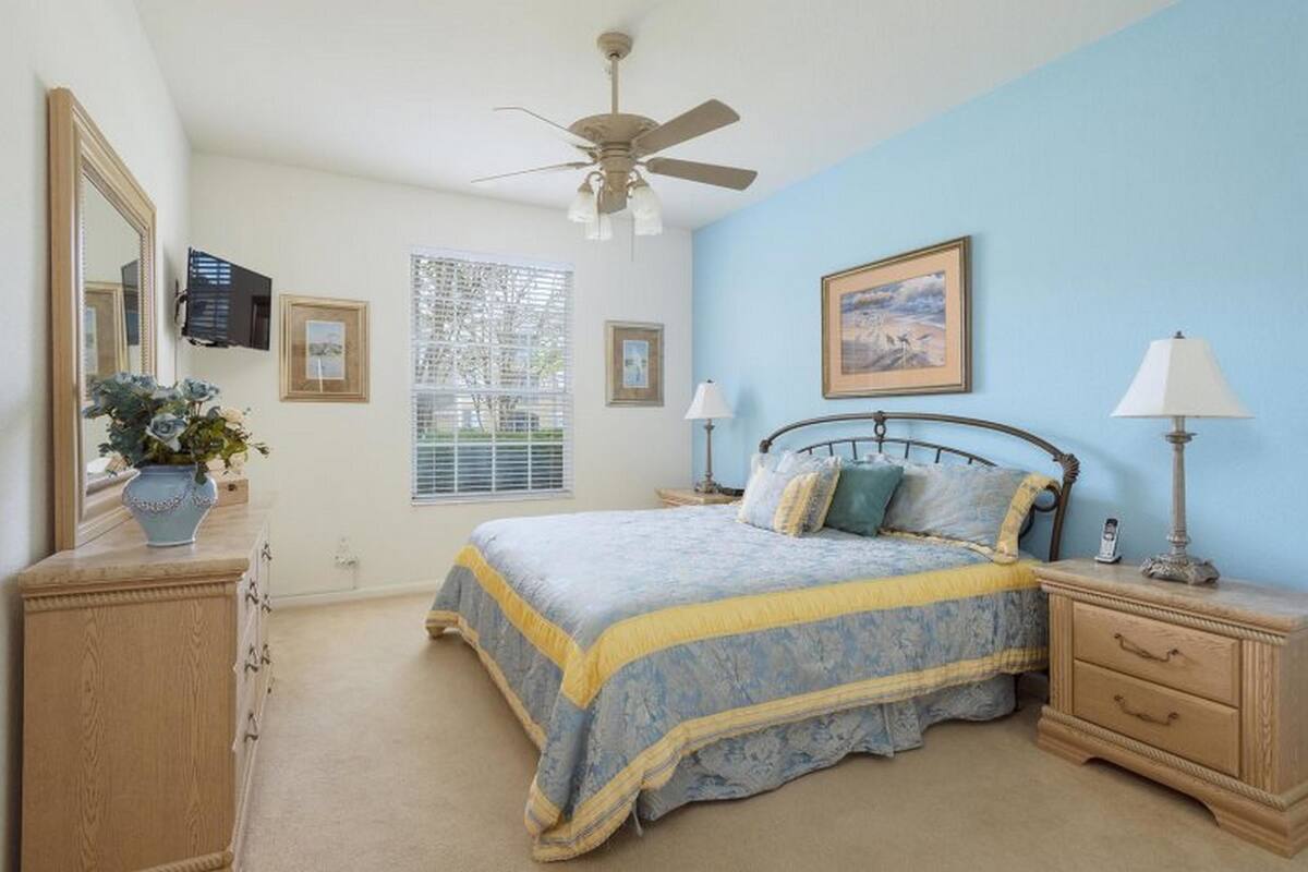 A bedroom with a bed, bedside tables, a ceiling fan, a window, and a mirror.