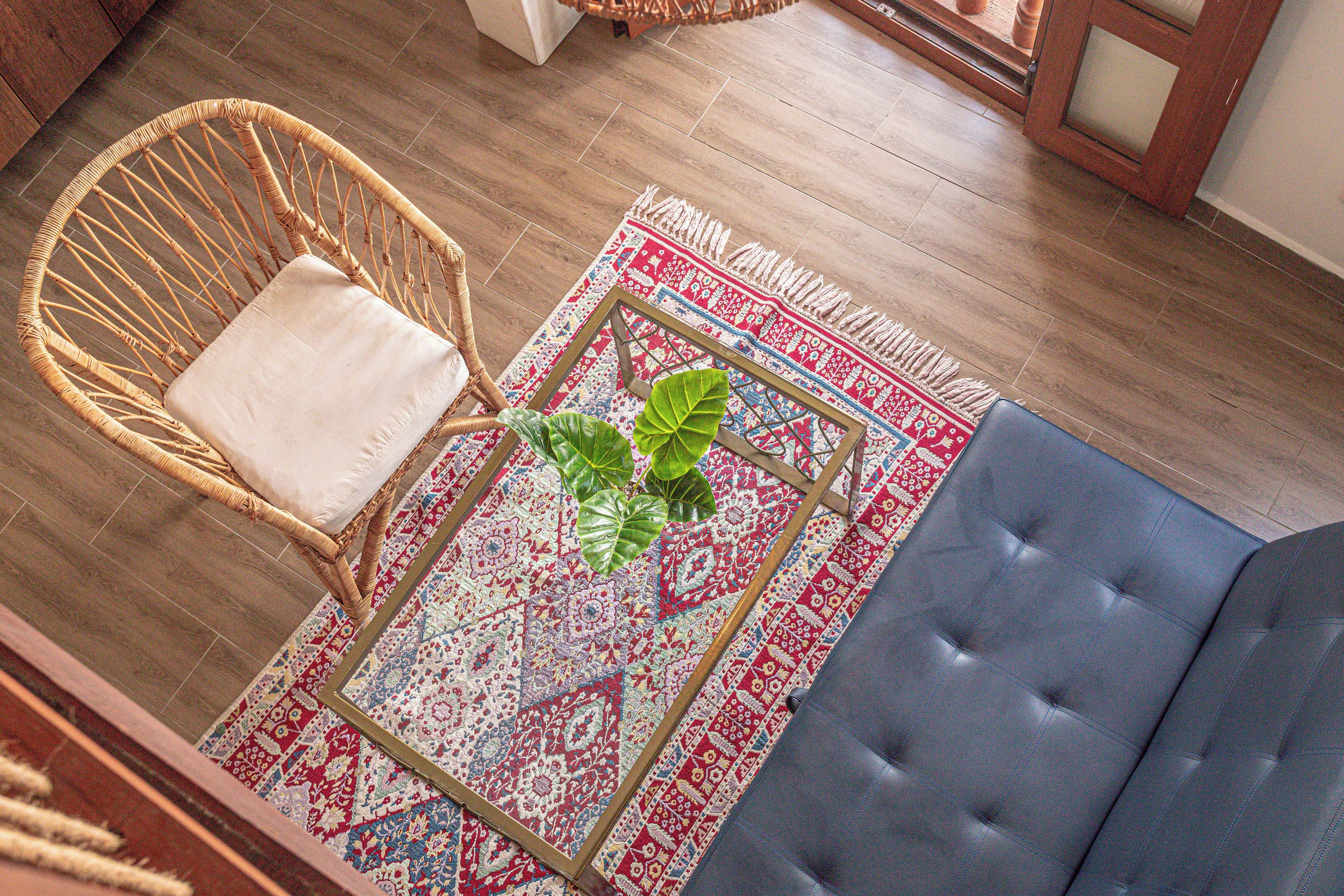 A wicker chair with a cushion, a blue sofa, and a patterned rug on a wooden floor.