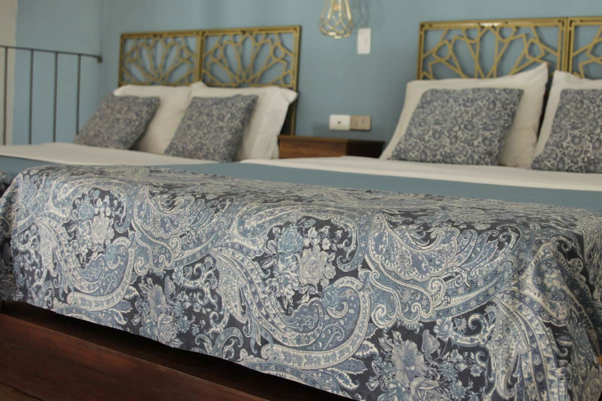 A bed with a patterned bedspread, a headboard with a geometric design, and a wall with a light switch.