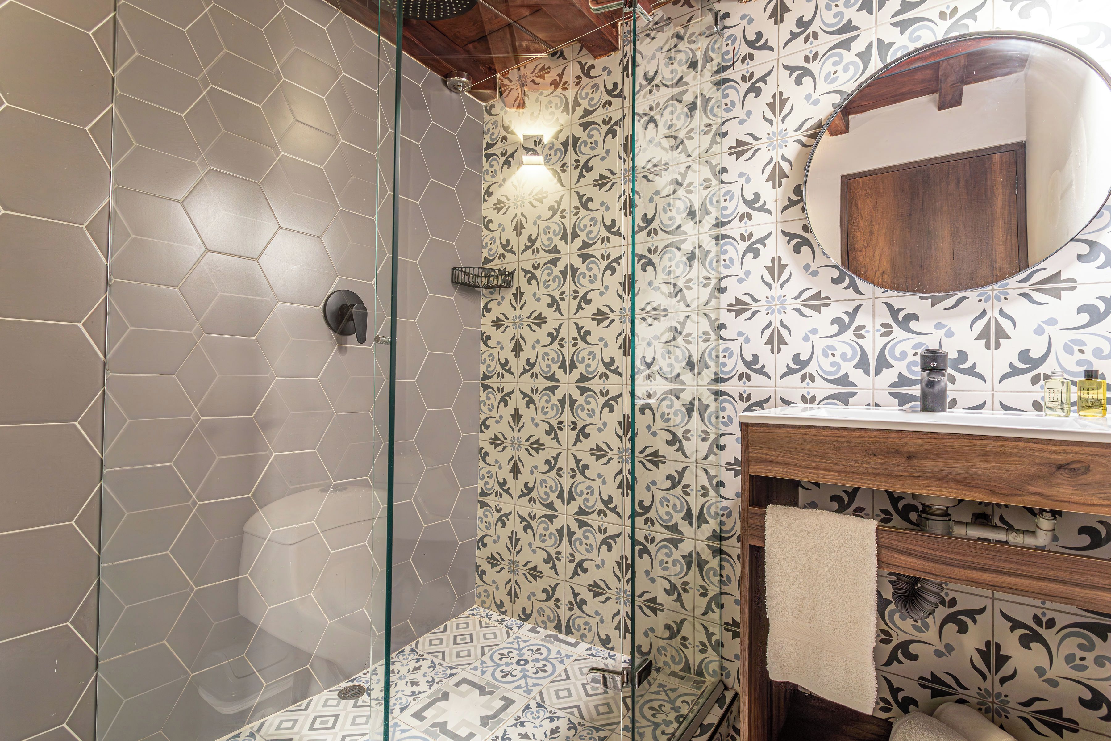 A bathroom with a glass shower enclosure, a wooden vanity with a mirror, and patterned tiles on the walls.