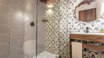 A bathroom with a glass shower enclosure, a wooden vanity with a mirror, and patterned tiles on the walls.