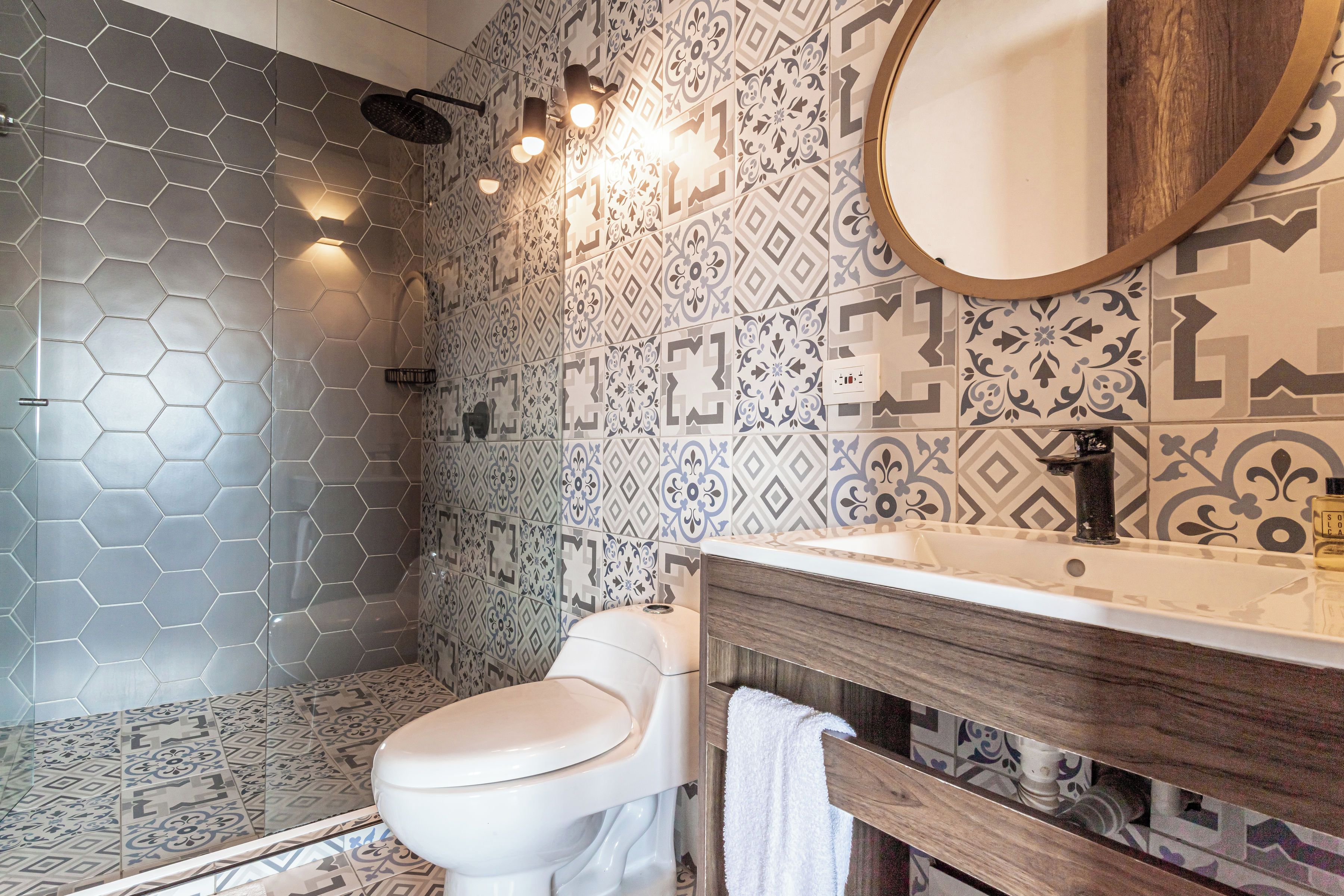Un baño con ducha de azulejos hexagonales, inodoro, lavabo con tocador de madera y espejo.