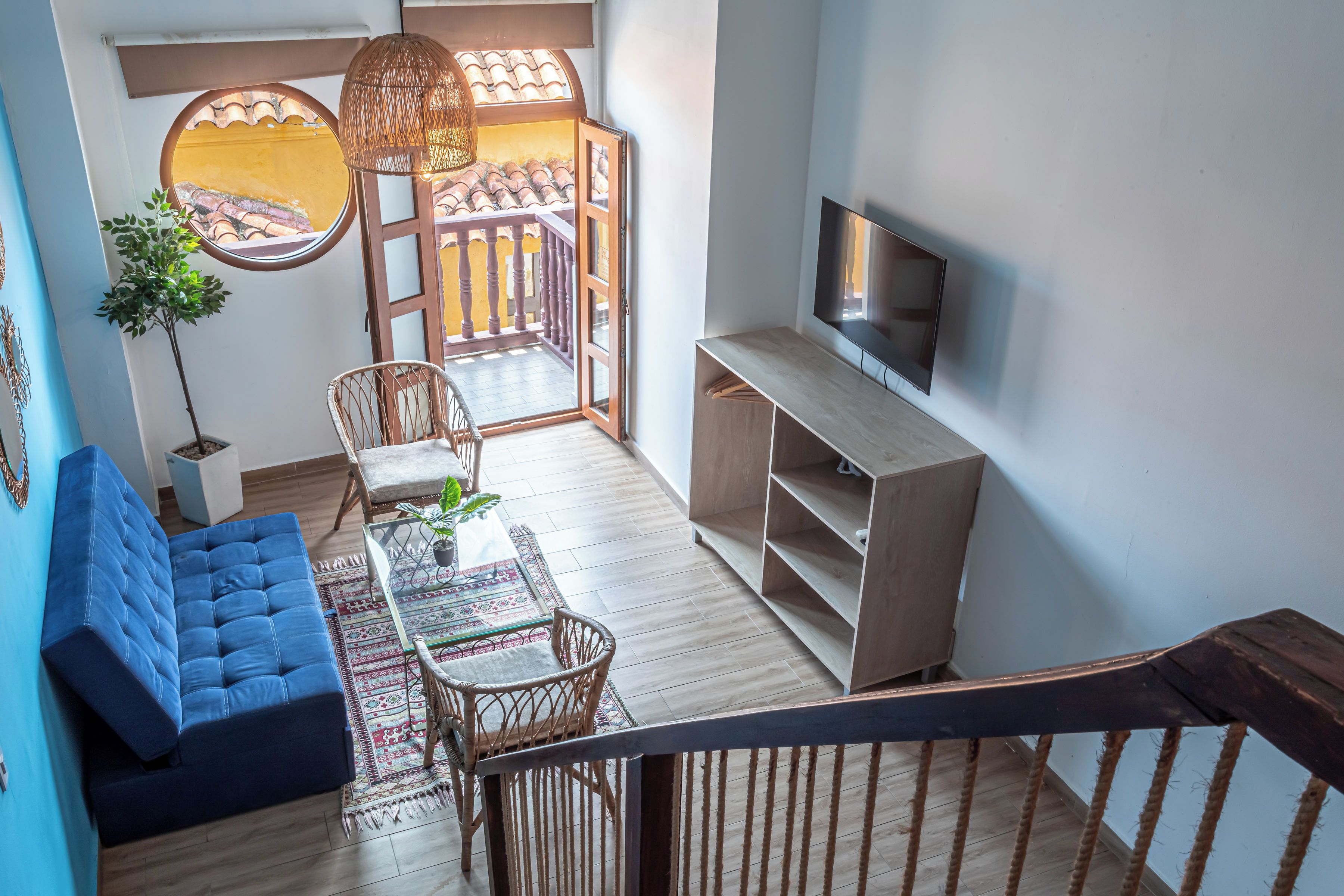 A modern living room with a blue sofa, a wooden TV stand, a dining table with chairs, and a balcony with a view.