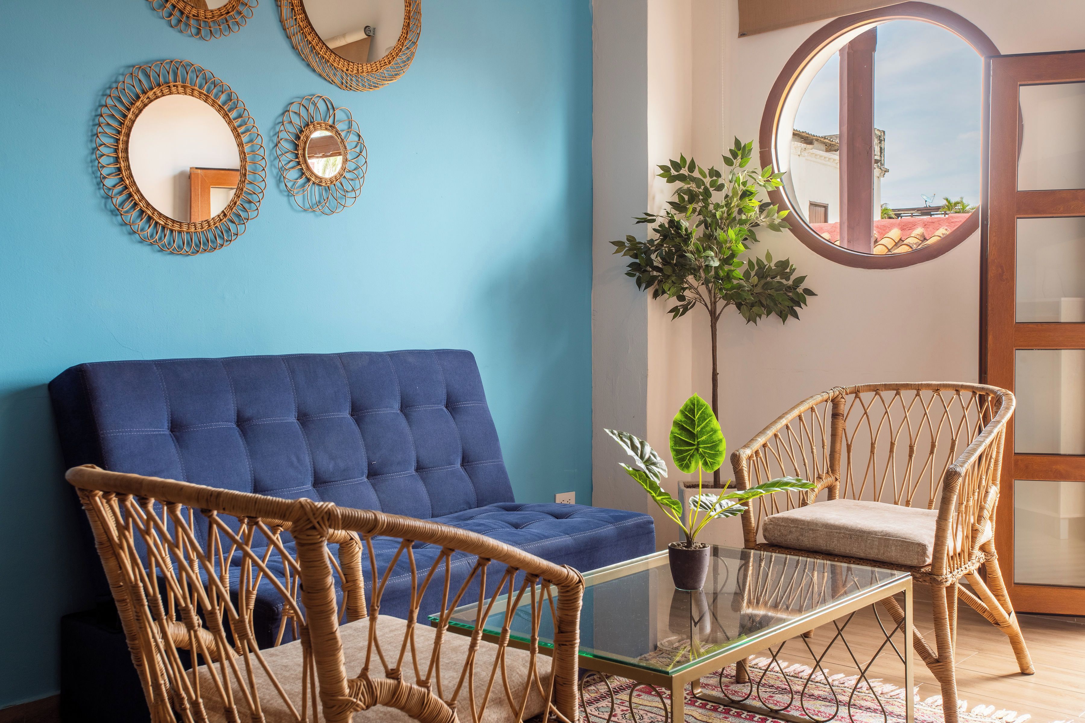 A room with a blue sofa, wicker chairs, a glass coffee table, and decorative mirrors on the wall.