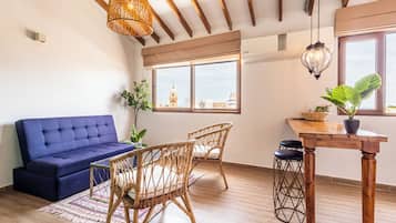 Una stanza con un divano blu, sedie in vimini, un tavolo di legno e vista su un edificio dalla finestra.