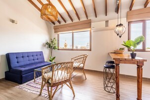A room with a blue sofa, wicker chairs, a wooden table, and a view of a building through the window.