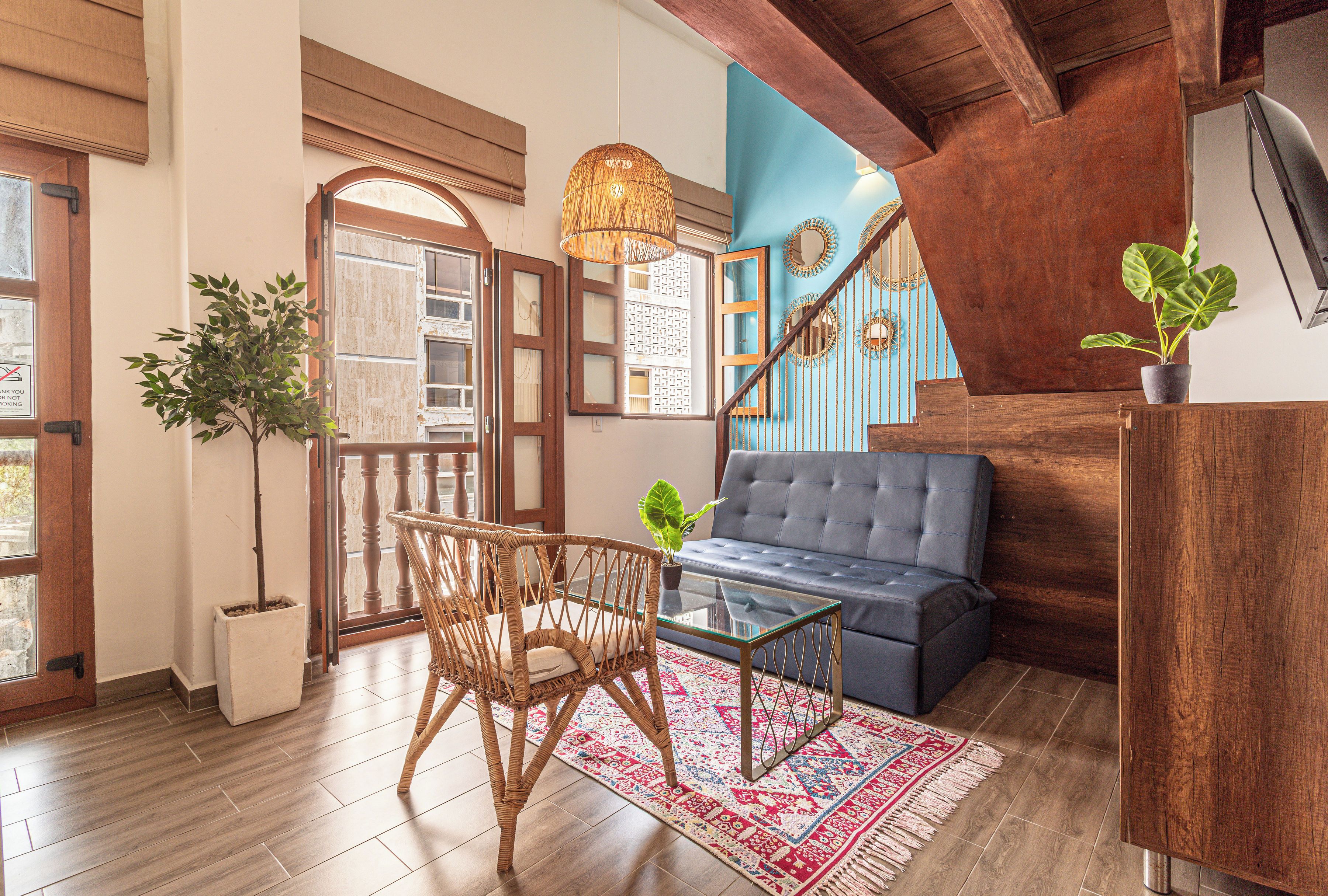 A room with a sofa, a glass coffee table, a wicker chair, a blue wall, and a wooden ceiling.