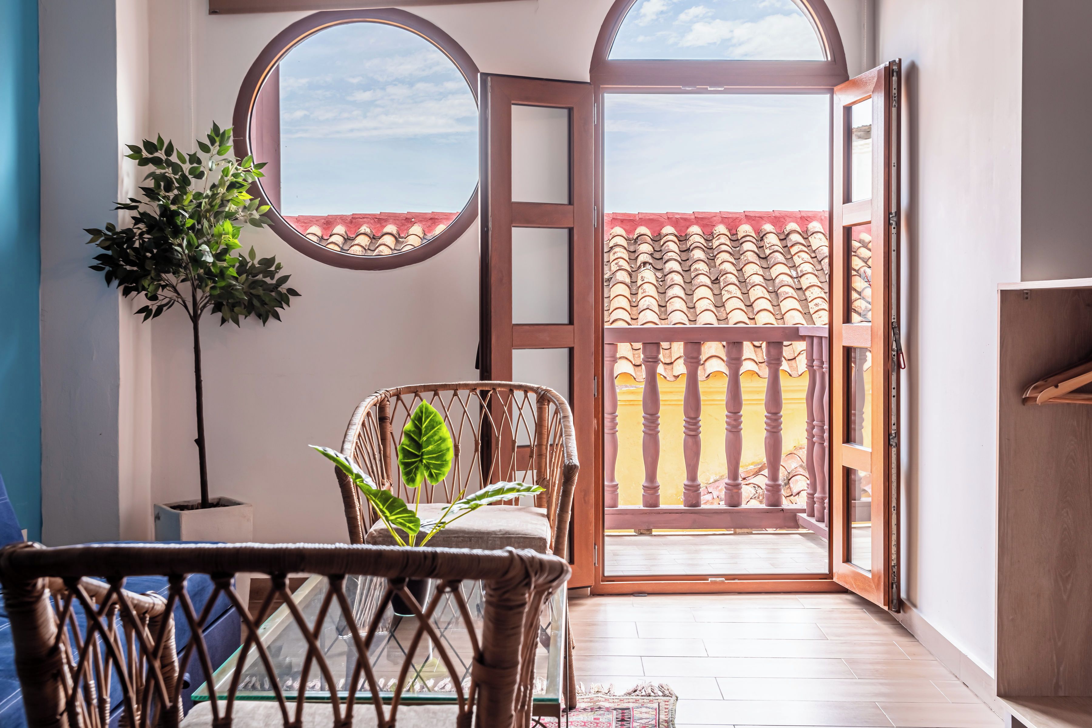 A room with a view of a tiled balcony, a wicker chair, a potted plant, and a wooden cabinet.