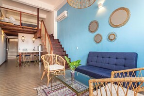 Una sala de estar con un sofá azul, sillas de mimbre, una mesa de centro y una escalera con barandilla de madera.