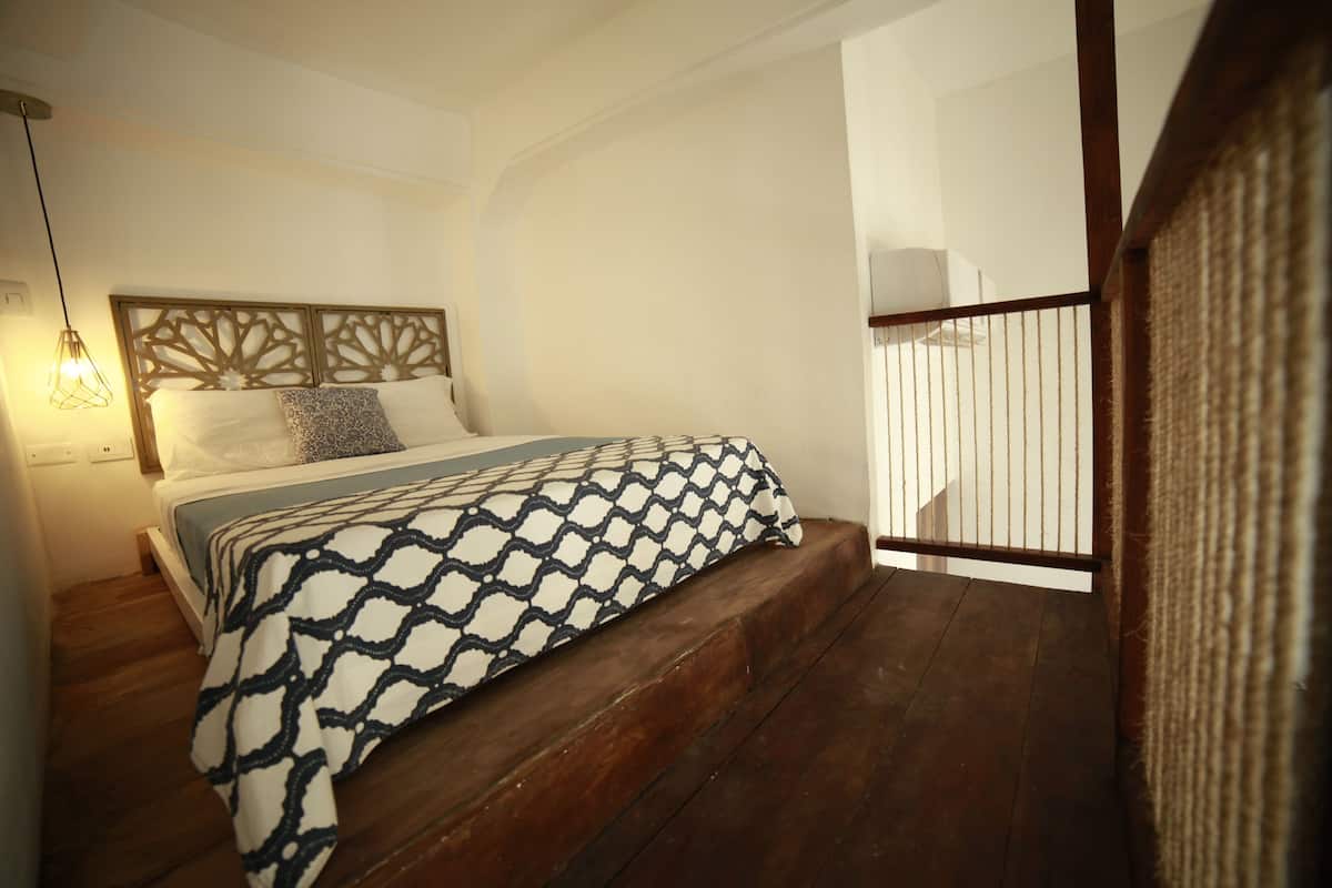 A bedroom with a bed, wooden floor, and a headboard with a geometric pattern.