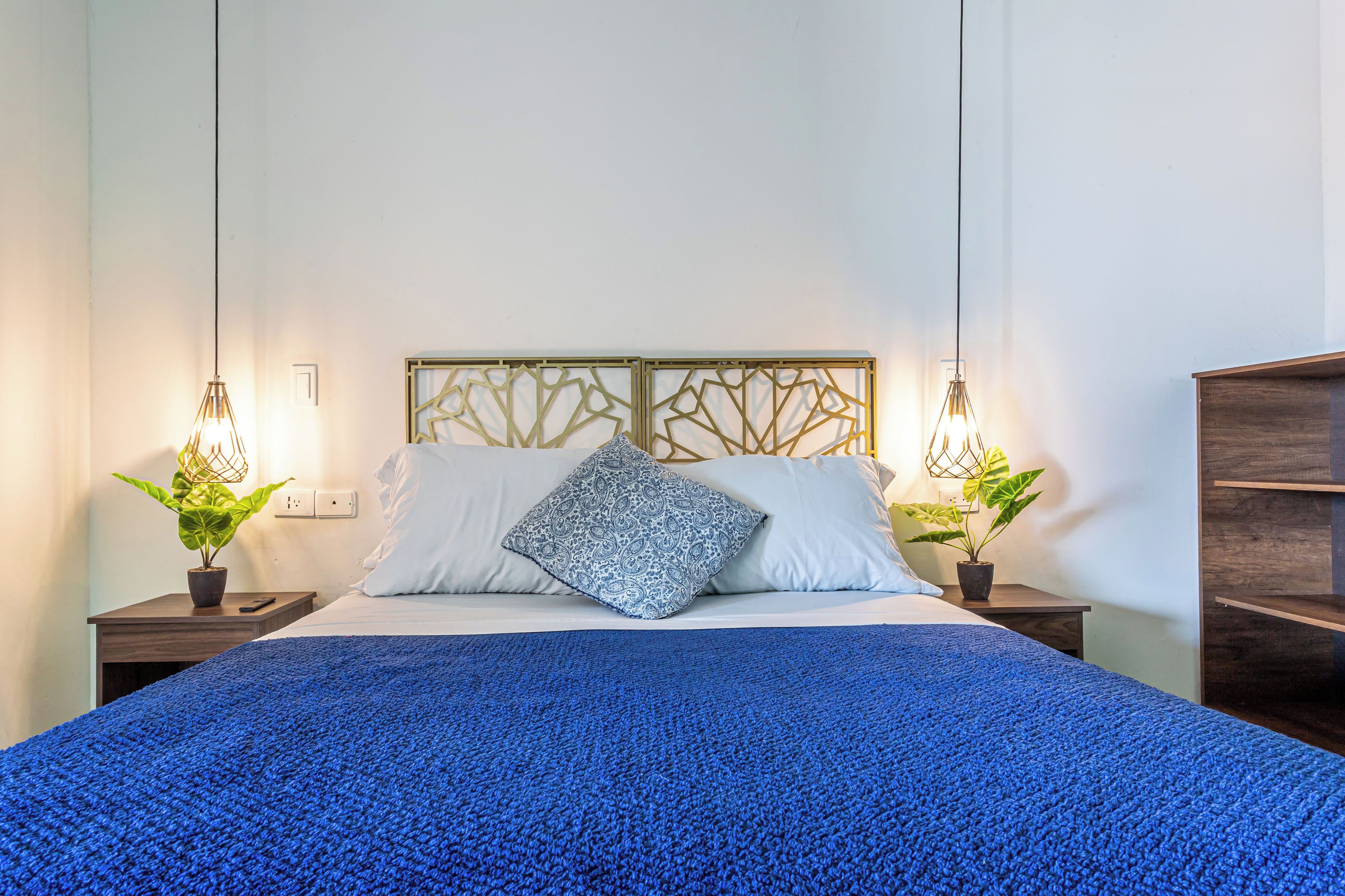 A bed with a blue blanket, two bedside tables with lamps, and a decorative headboard.