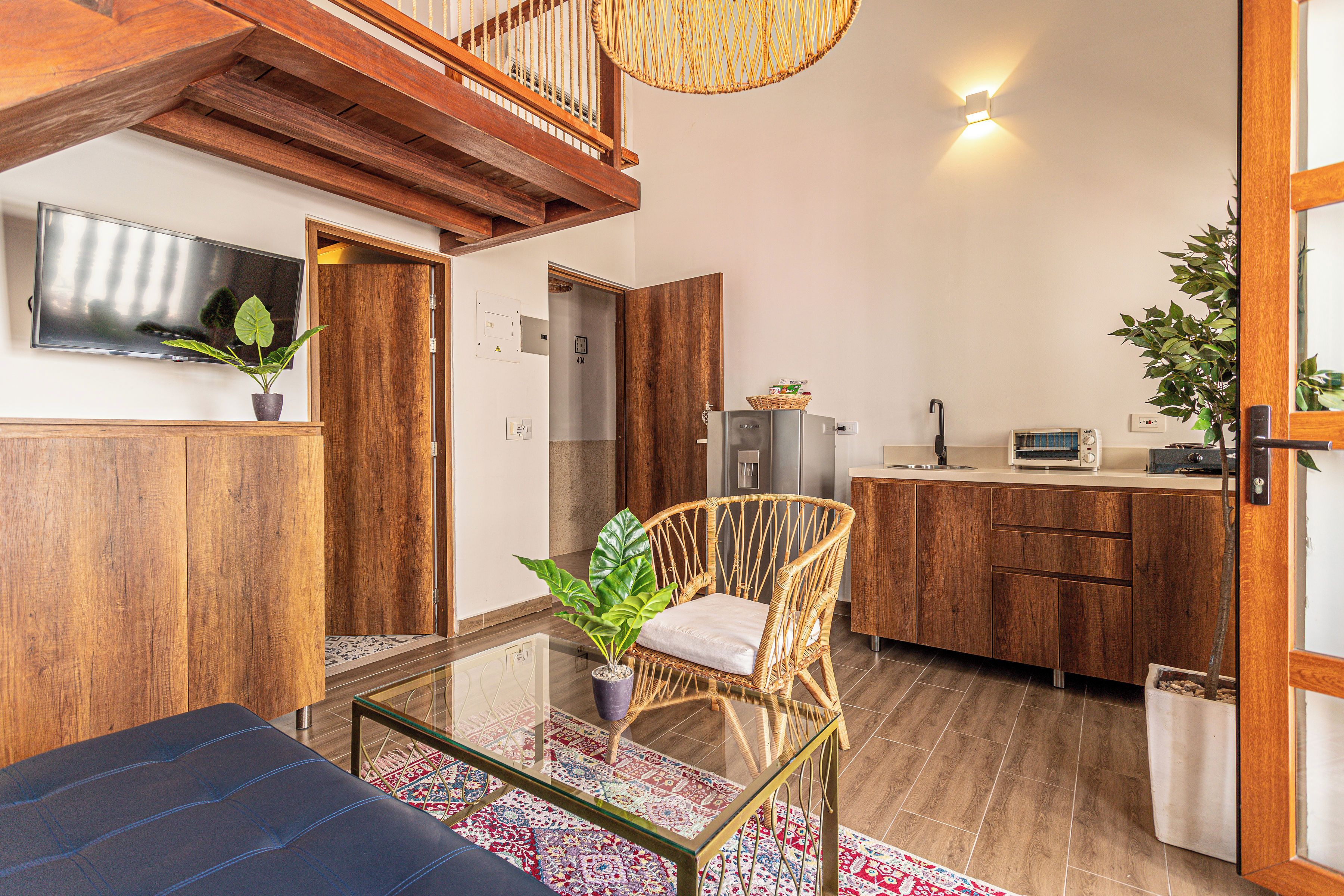 A modern interior with a glass coffee table, wicker chair, and a kitchen area with wooden cabinets.