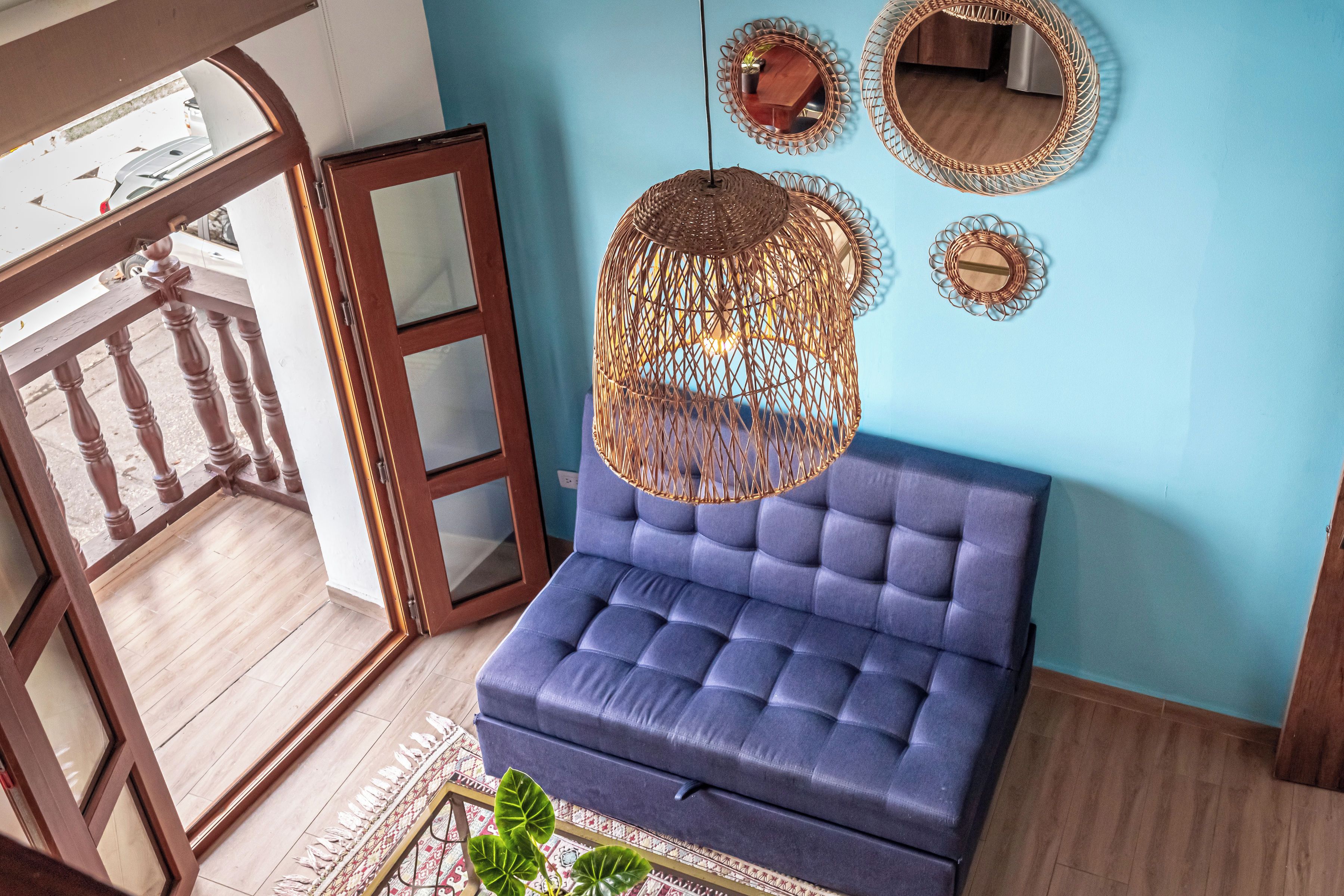 Una habitación con un sofá azul, una lámpara colgante y espejos decorativos en la pared.