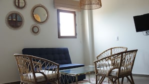 Una sala de estar con un sofá azul, sillones de mimbre, una mesa de centro de vidrio y una lámpara de techo tejida.