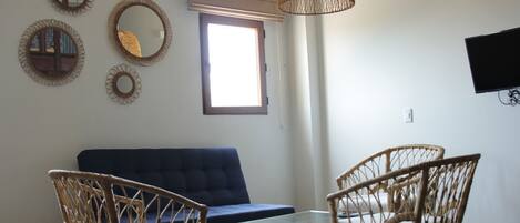 A living room with a blue sofa, wicker chairs, a glass coffee table, and a woven light fixture.