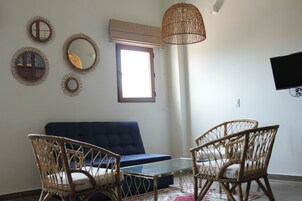 Una sala de estar con un sofá azul, sillones de mimbre, una mesa de centro de vidrio y una lámpara de techo tejida.