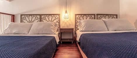 Une chambre d’hôtel avec deux lits, un plancher en bois, une table de chevet avec une lampe et une tête de lit décorative.