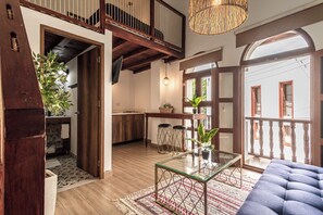 A spacious living area with a high ceiling, a glass coffee table, a blue sofa, and a large window with a view of the outside. - Soy Local Centro Historico (Cartagena)