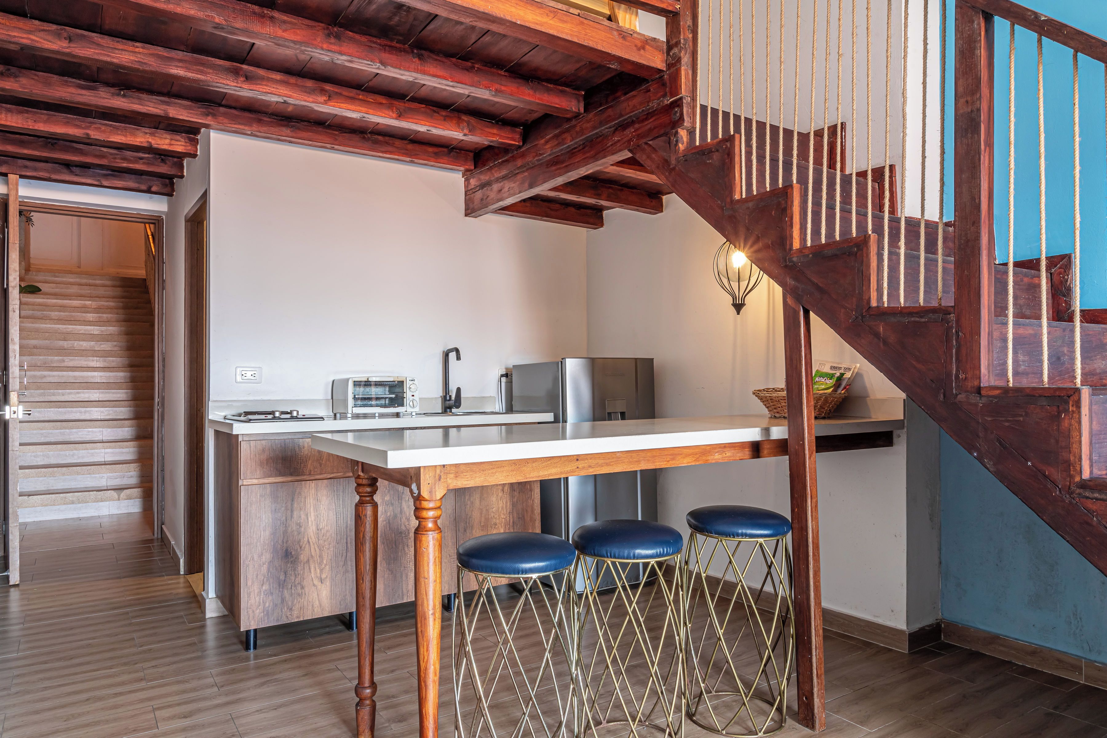 A kitchen with a wooden table, bar stools, and a staircase with a wooden railing.