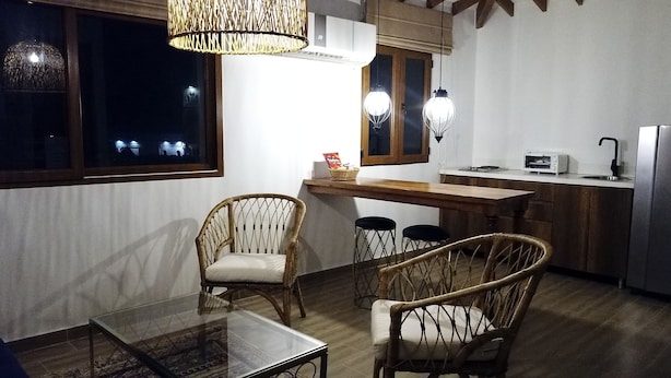 Una cocina compacta con comedor, que presenta mobiliario de mimbre, una mesa de vidrio y lámparas colgantes.