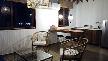 Una cocina compacta con comedor, que presenta mobiliario de mimbre, una mesa de vidrio y lámparas colgantes.