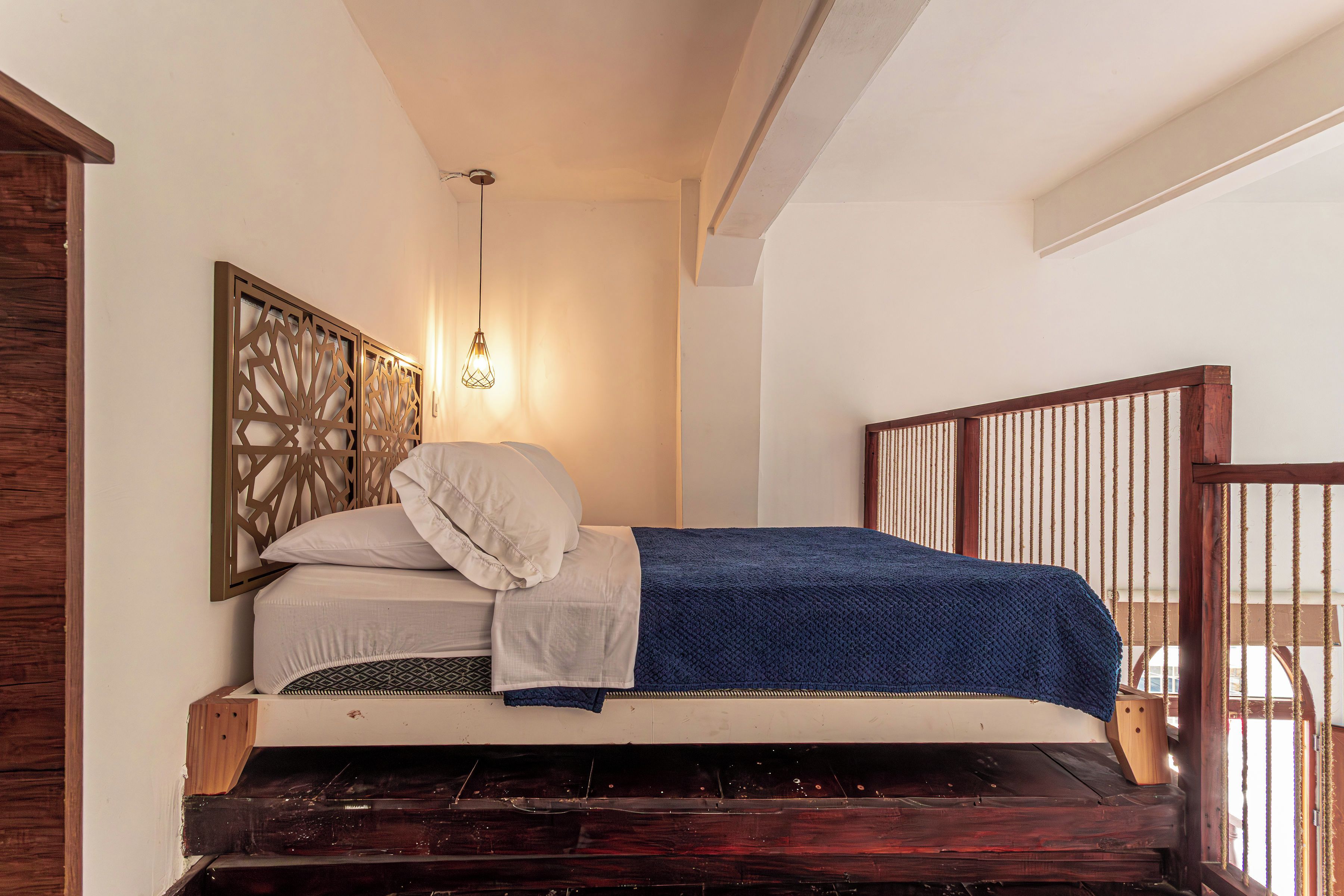A single bed with a wooden headboard, a white pillow, a blue blanket, and a wall-mounted light fixture.